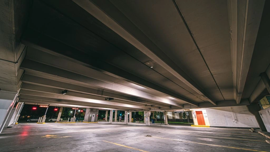 A freshly sealcoated commercial parking lot at dawn with crisp line striping and a sealcoat tanker on site